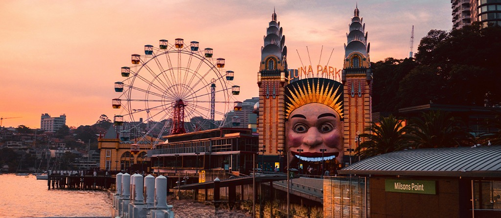 Luna Park Sydney and its Ferris wheel glowing at sunset beside Sydney Harbour at Milsons Point.