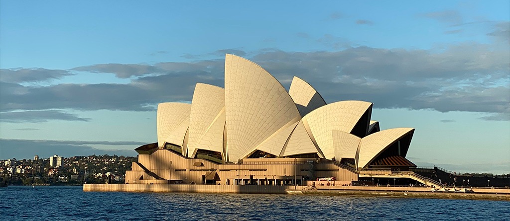 Sydney Opera House viewed from the harbour at Circular Quay during golden hour beside the waterfront. 